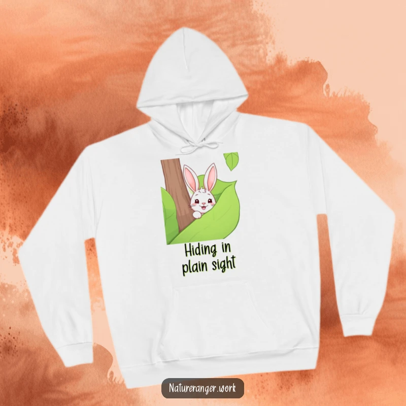 Funny hoodie illustration of a playful cartoon rabbit stealthily peeking out from behind a large forest leaf.